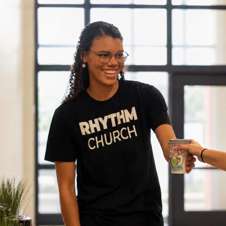 A Rhythm Church volunteer smiling while handing someone coffee on Sunday morning